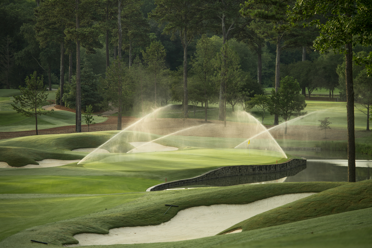 Bild eines Golfplatzes, auf dem eine automatische Bewässerungstechnik steht, die gerade Wasser versprüht